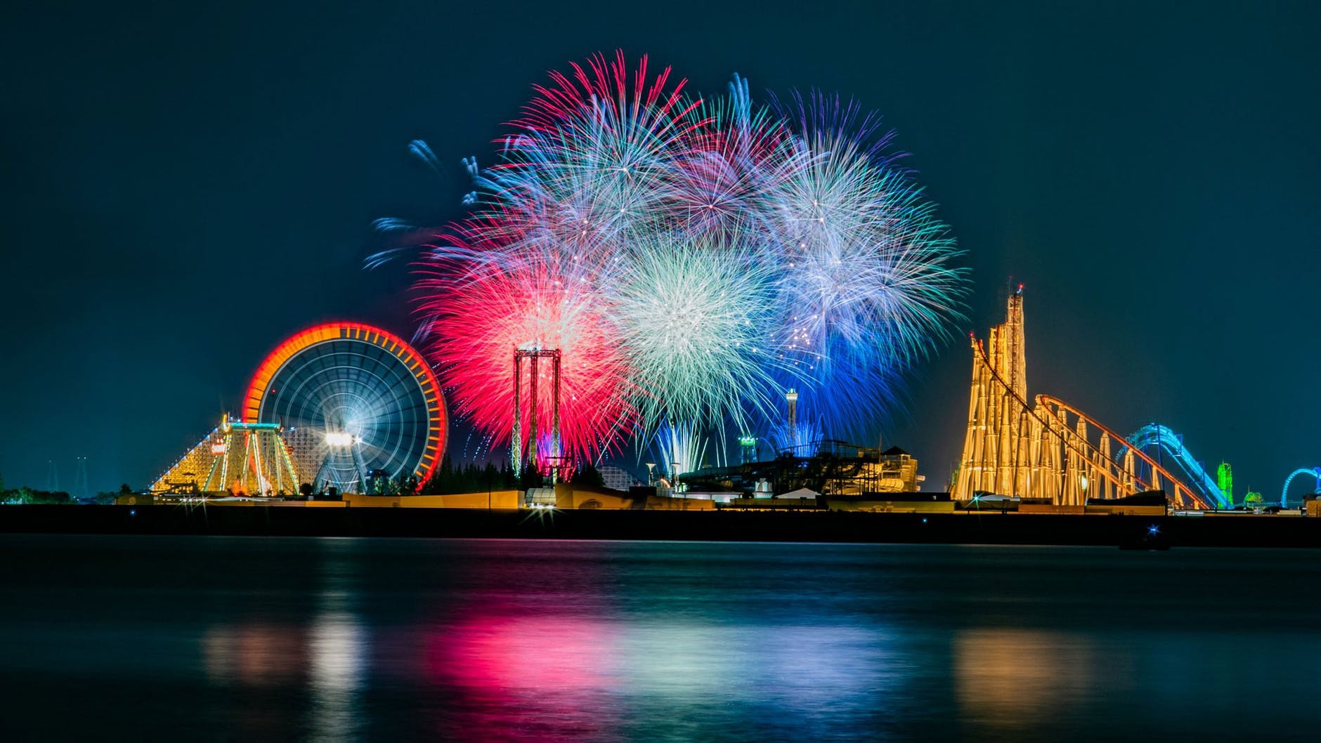 bright fireworks in sky over amusement park and lake